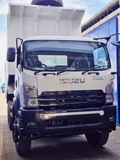Front view of a white Isuzu FVZ BluePower tipper truck parked at a dealership, featuring a heavy-duty dump body and rugged commercial design.