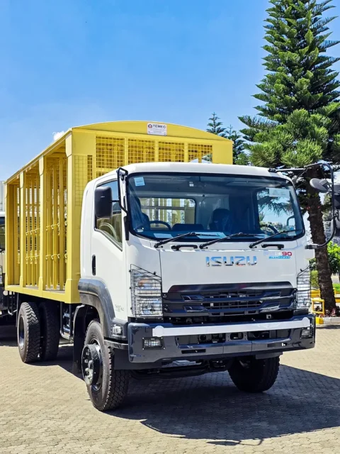 Isuzu FVR 90 Blue Power truck with a yellow livestock body parked outdoors near trees.