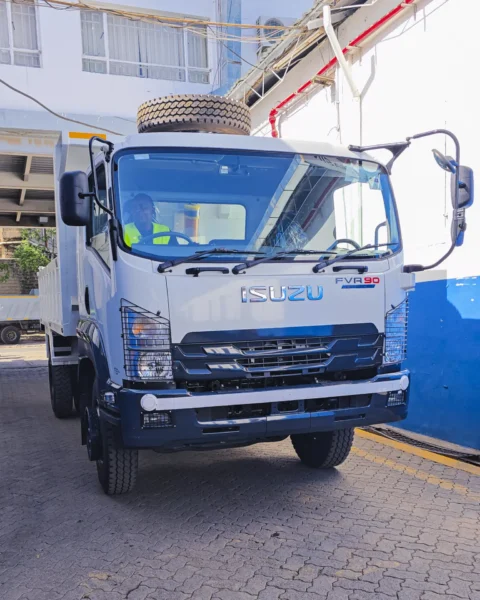 Front view of a white Isuzu FVR 90 tipper truck parked outside a building.