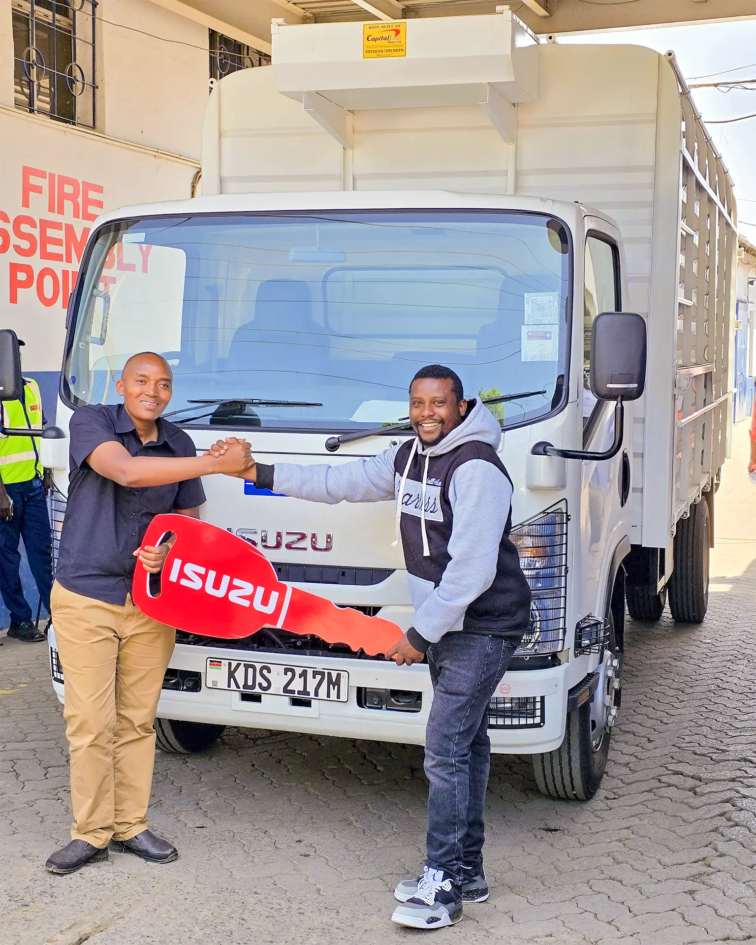 Gerald Kibuthi Maina receiving his brand-new Isuzu NQR 81 BLUEPOWER Truck from Wang'ombe, a top sales representative at Isuzu Kenya, during the handover ceremony.