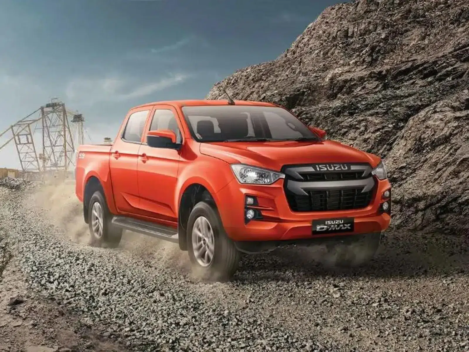 An orange Isuzu D-Max pickup truck navigating a rugged, rocky off-road terrain, kicking up dust