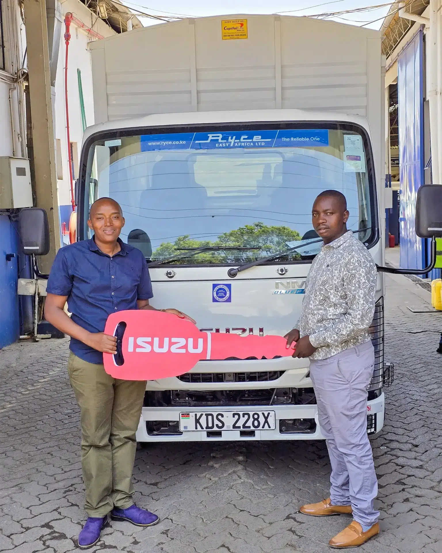 Wang'ombe, a top Isuzu sales representative in Kenya, handing over a symbolic Isuzu key to JIGEN FAVOUR in front of a newly purchased Isuzu NMR BLUEPOWER Truck.