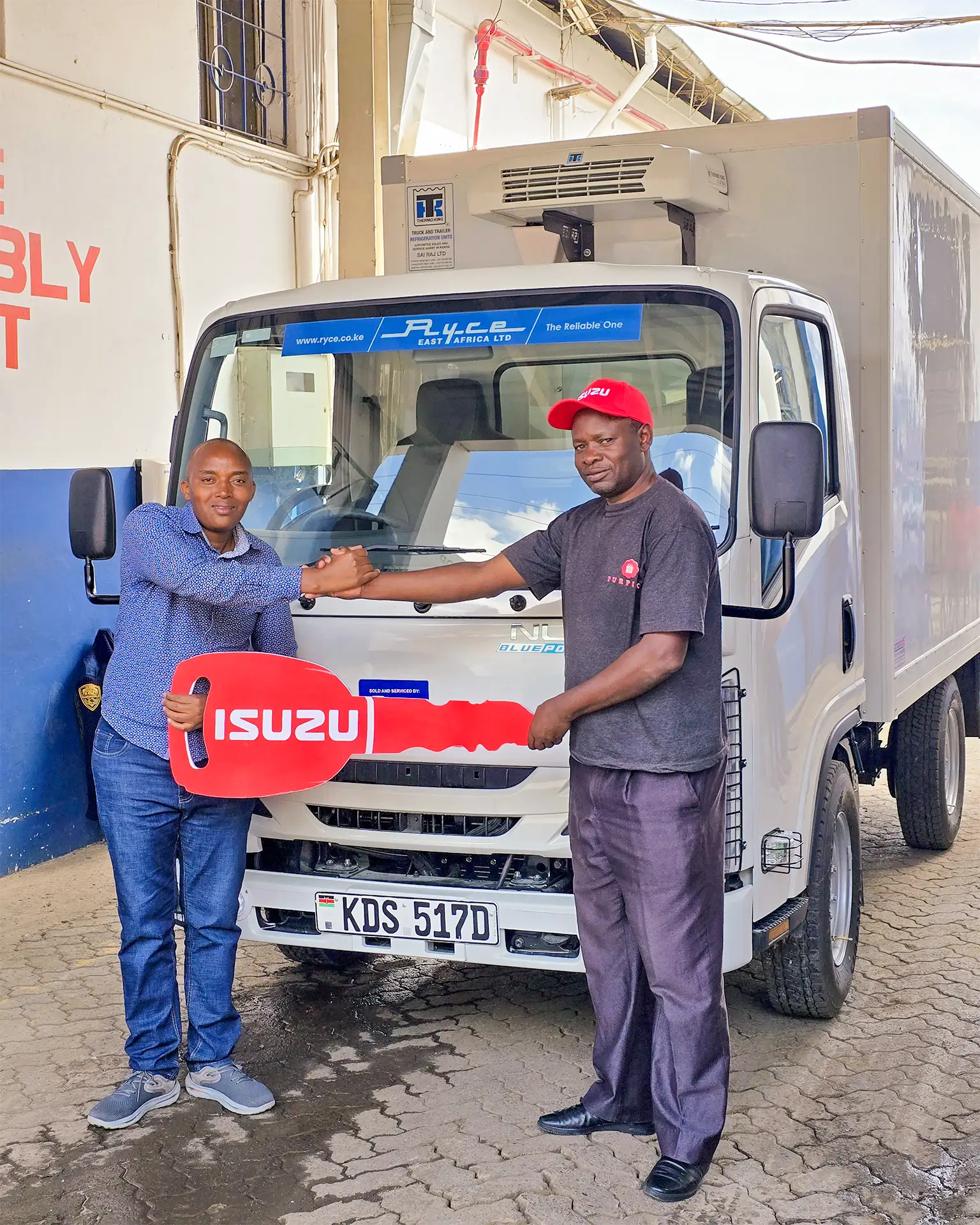 Wang'ombe, a top Isuzu sales representative, shaking hands with a satisfied customer from PURPINK GIFTS LTD while presenting the keys to a brand-new Isuzu NLR BLUEPOWER Truck. The white truck is prominently displayed in the background with the license plate "KDS 517D," showcasing its modern design and reliability.